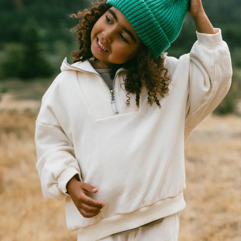 Person wearing a white fleece pullover and green knit beanie in an outdoor setting