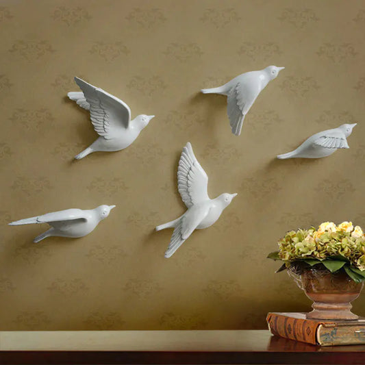White bird wall decorations on a patterned wall with a vase of flowers and books below.