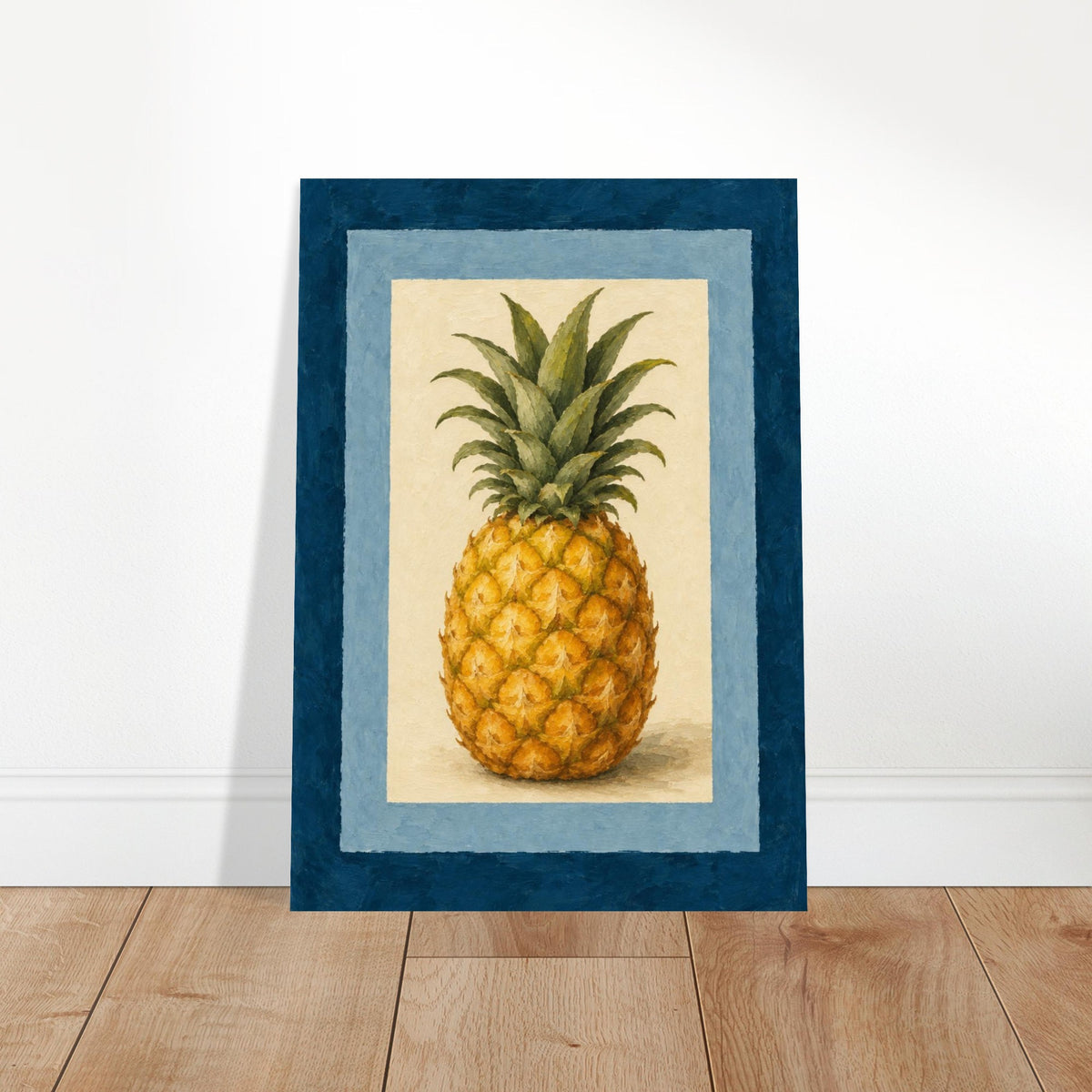 A framed art print featuring a detailed illustration of a yellow pineapple with green leaves, set against a cream background with layered blue borders, leaning against a white wall on a light wood floor.