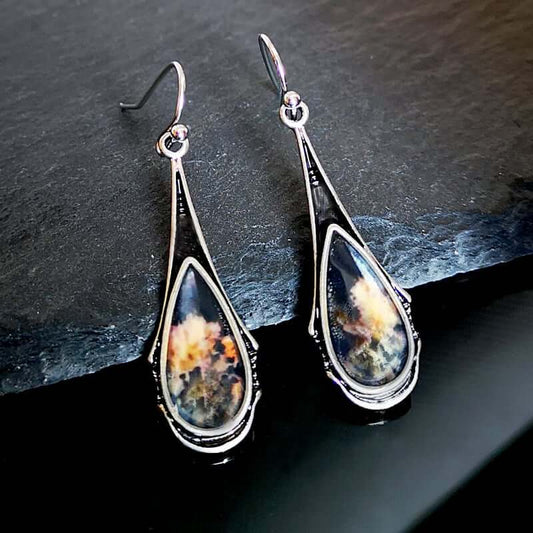 Teardrop-shaped earrings with a celestial design on a dark surface