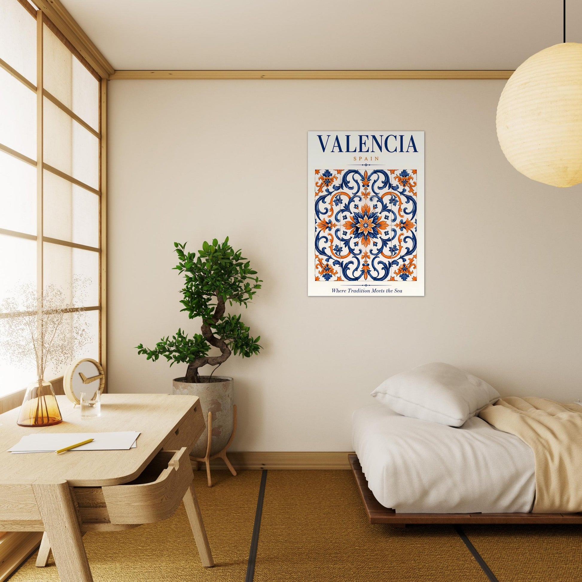A framed poster with a blue, orange, and white ornamental tile pattern and the word 'VALENCIA' at the top, displayed on a beige wall in a modern Japanese-style room with a bed, desk, and plant.