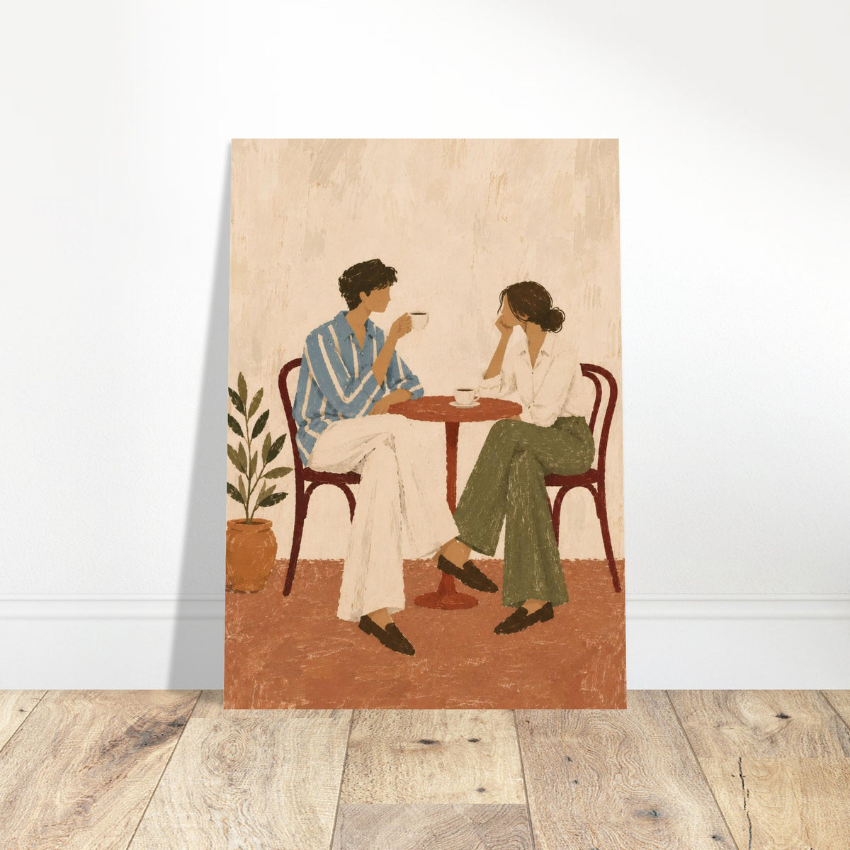 A vertical art print depicting a couple in a cafe setting, leaning against a white wall on a light wood floor. The print features a textured, vintage-style illustration of two people sitting at a small table with coffee cups, with a potted plant on the left.