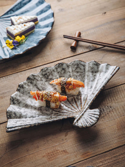 Japanese ceramic fan-shaped sushi plate with a solid glaze finish, displayed on a rustic dining table setting