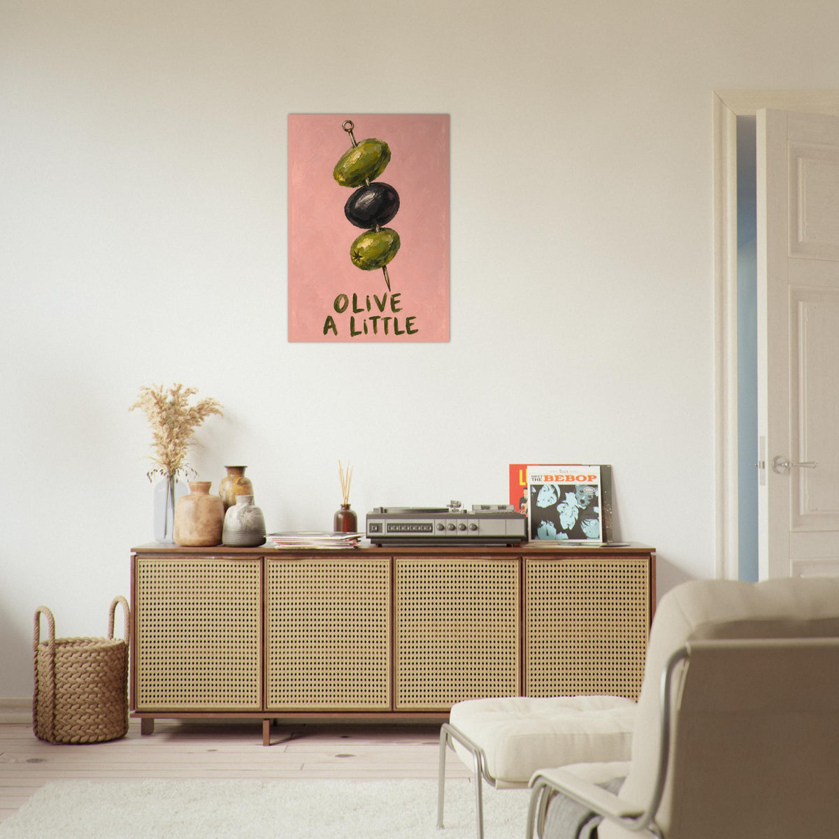 Olive a Little print above a woven-front sideboard in a neutral living room, with decorative vases and a pale armchair.