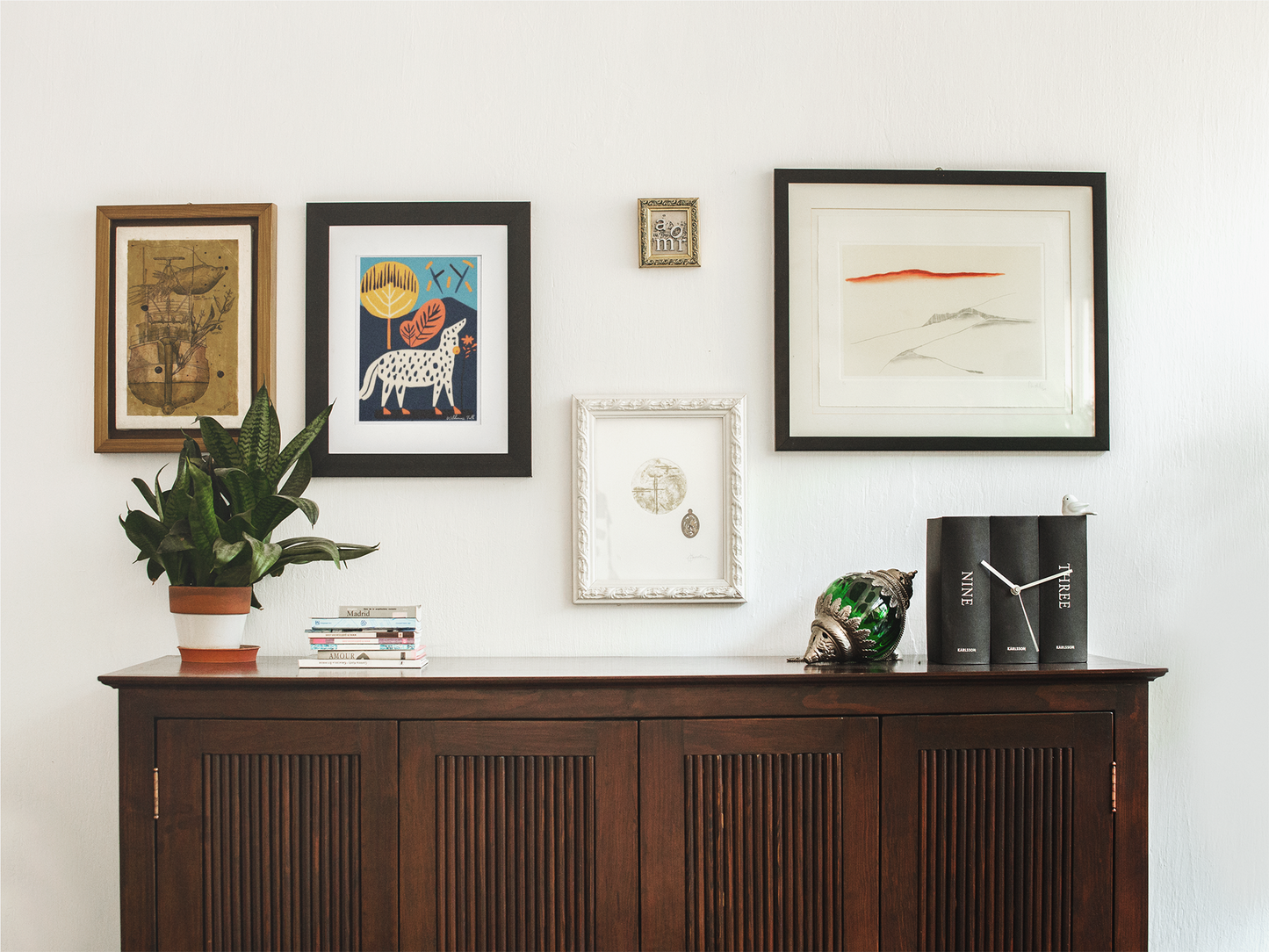 Wooden sideboard with framed artwork and decorative items against a white wall