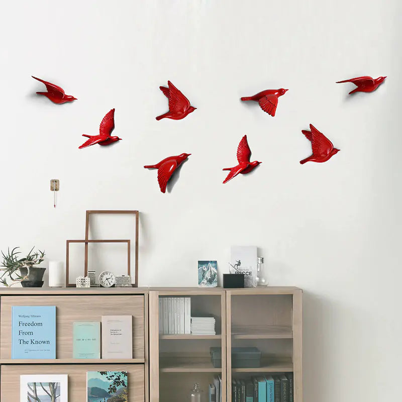 Red bird-shaped decorations on a white wall above a wooden cabinet with books and decor items.
