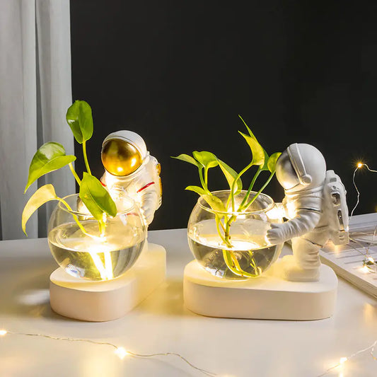 Two decorative items with astronaut figures holding plants in glass jars on a table.