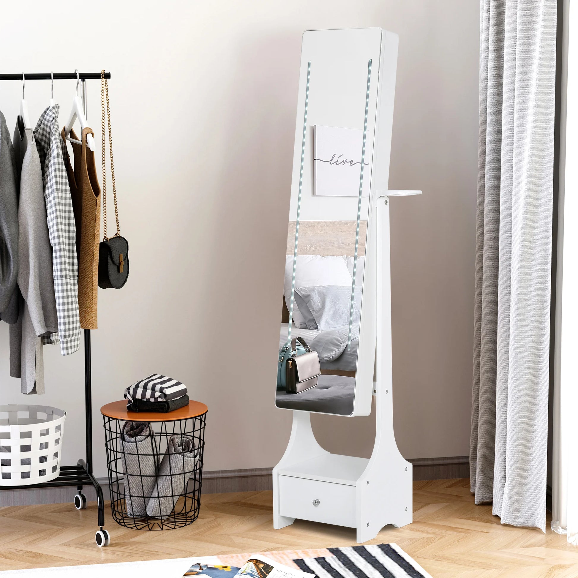 White standing mirror with a shelf in a room with clothes and a basket.