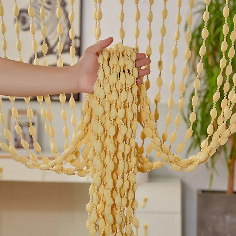 Hand holding a yellow beaded curtain with a blurred indoor background