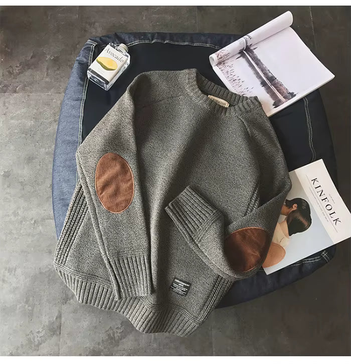 Gray sweater with brown patches on a surface with magazines and a bottle.