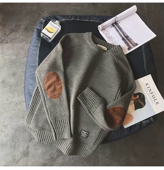 Gray sweater with brown patches on a surface with magazines and a bottle.