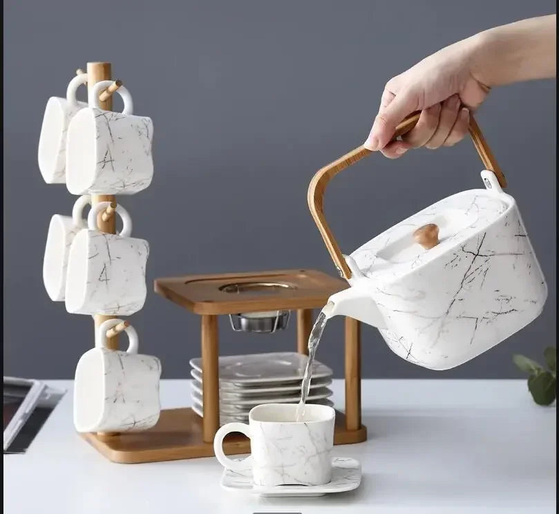 Person pouring tea from a marble-patterned teapot into a cup with a marble-patterned mug rack in the background.
