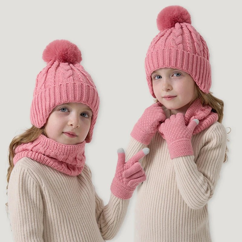 Two children wearing pink knit hats, scarves, and gloves on a light background