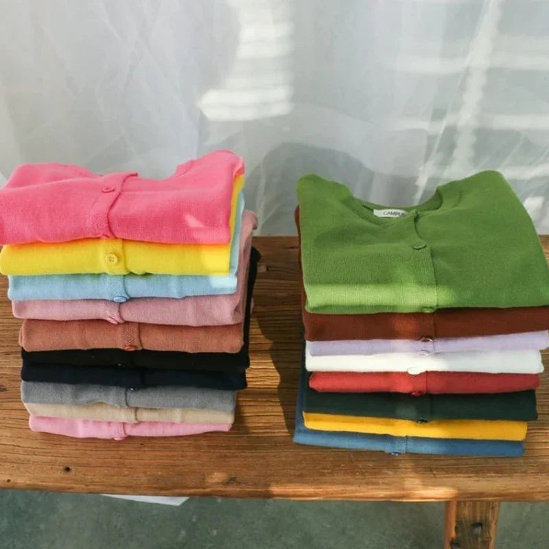 Stacks of colorful polo shirts on a wooden table with a white curtain background.