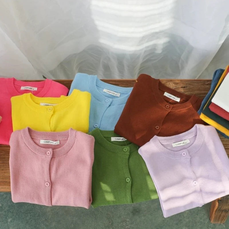 Folded children's cardigans in various colors on a wooden surface.