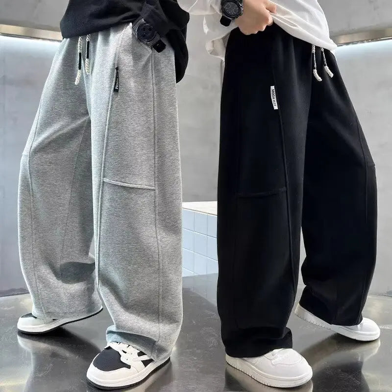 Two pairs of wide-leg pants, one gray and one black, worn by people on a reflective surface.