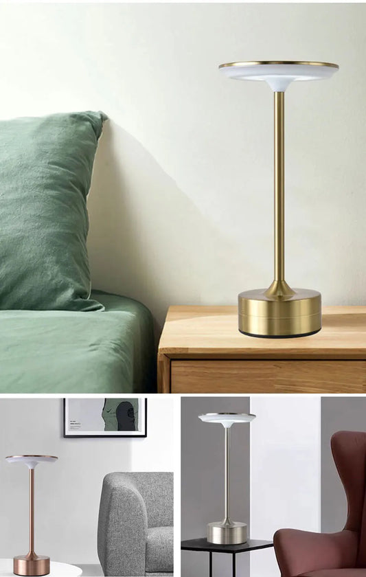 Gold table lamp on a wooden surface with a green cushioned chair in the background.