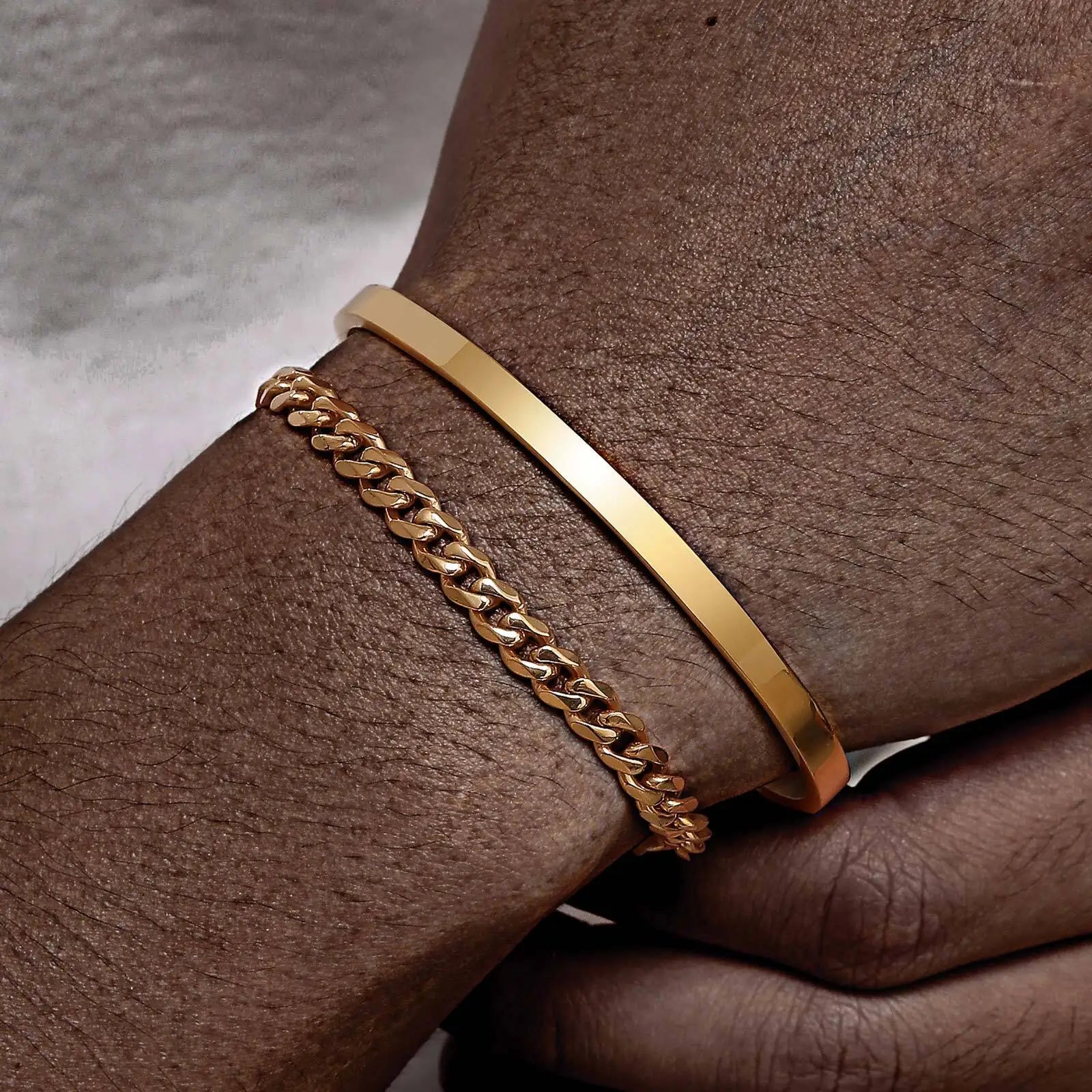Gold bracelet and chain on a wrist against a neutral background