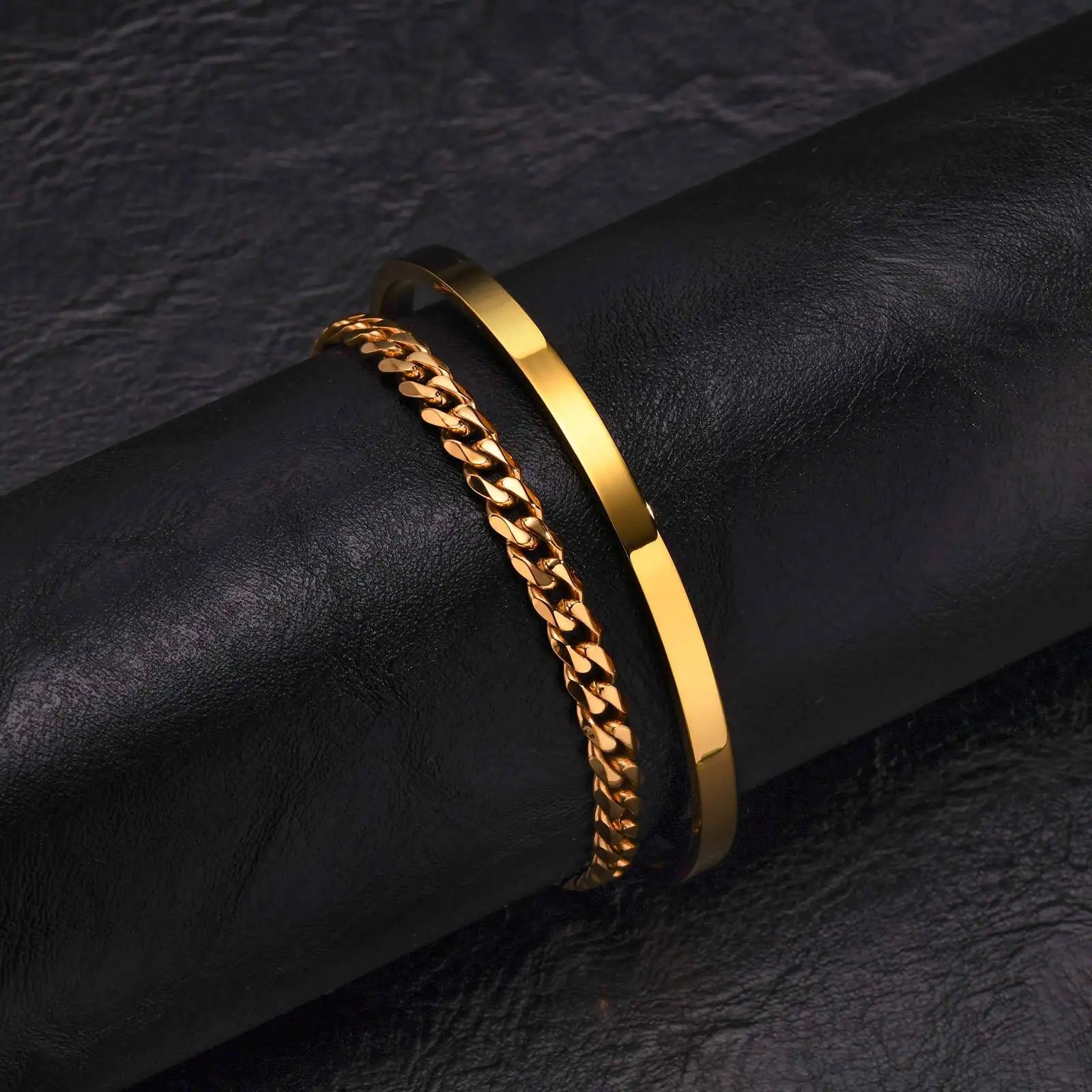 Two gold bracelets on a black leather surface