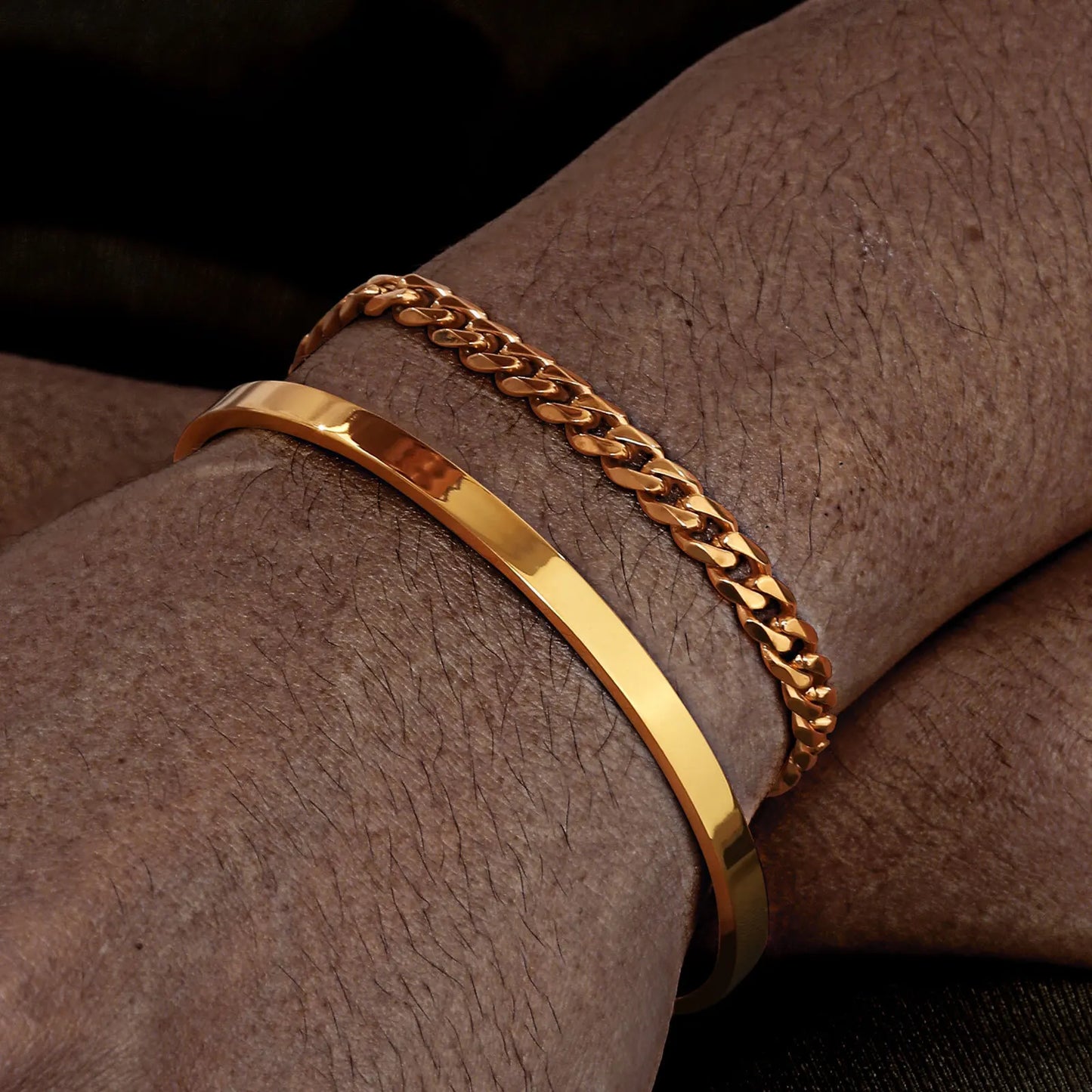 Two gold bracelets on a wrist against a dark background