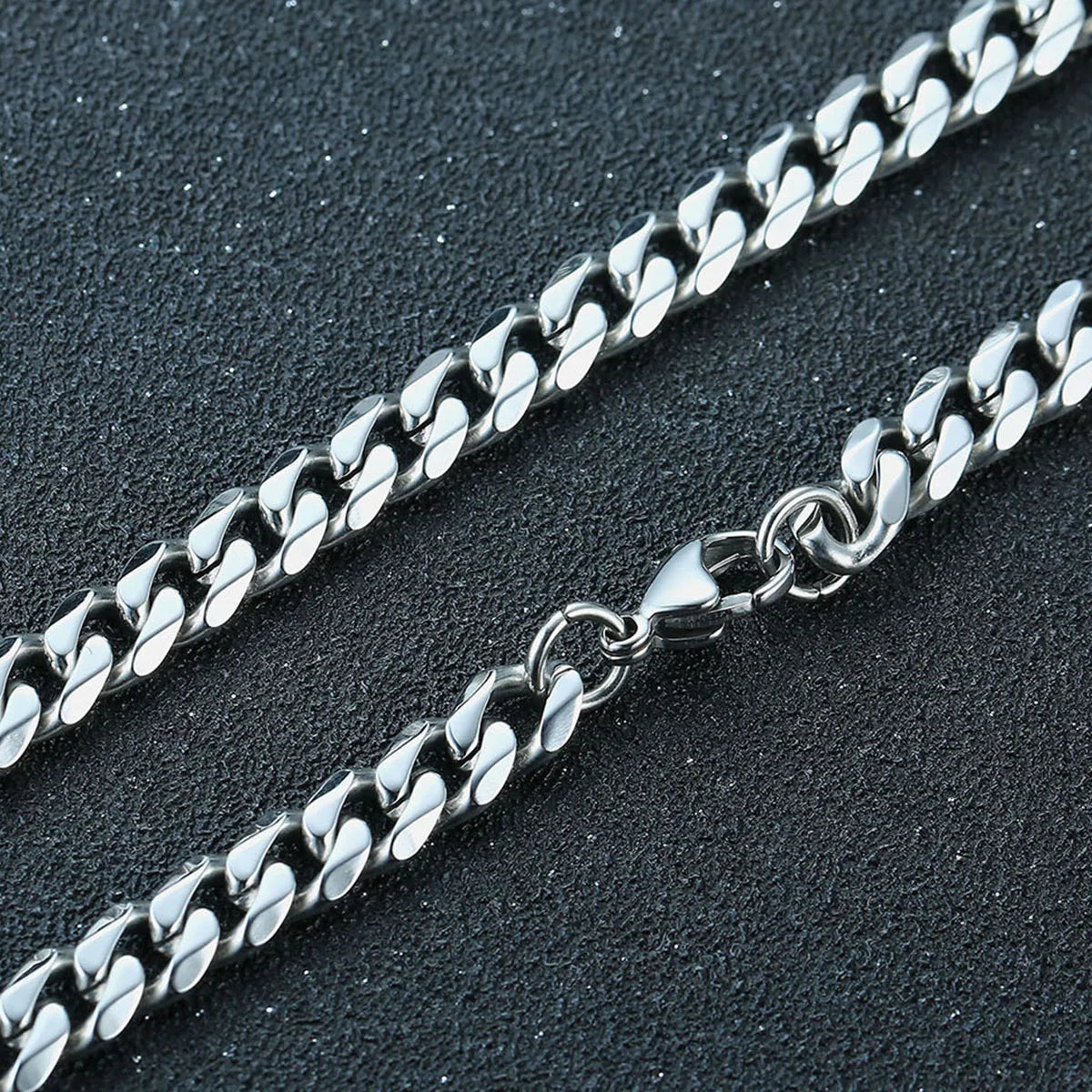 Two silver chain necklaces on a dark textured surface