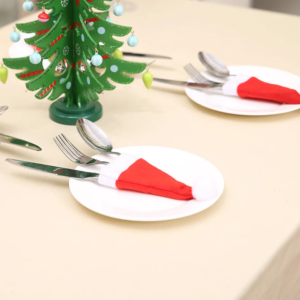 Table setting with white plates, red napkins, silverware, and a small green Christmas tree on a beige surface.
