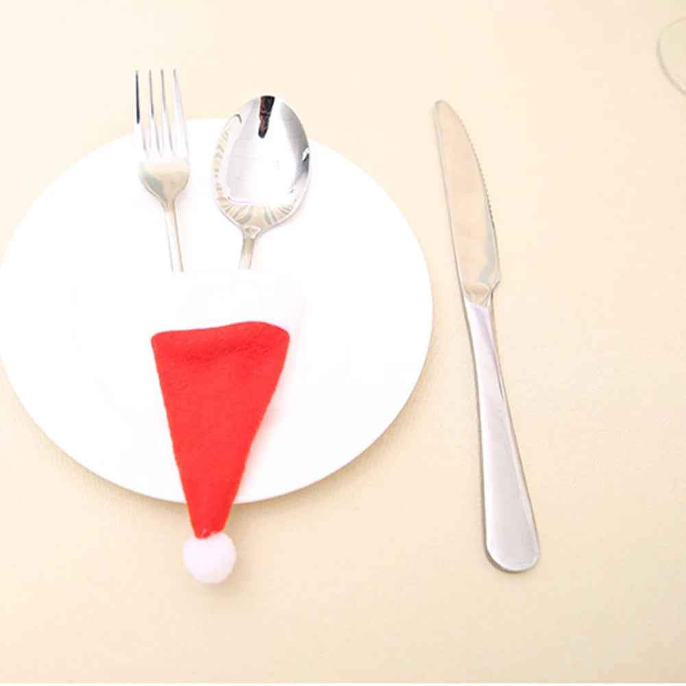 White plate with a red Santa hat, silver fork, spoon, and knife on a beige background