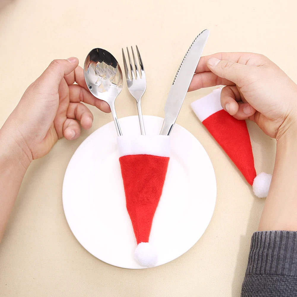 Santa hat cutlery holders on a white plate with hands holding a spoon, fork, and knife.