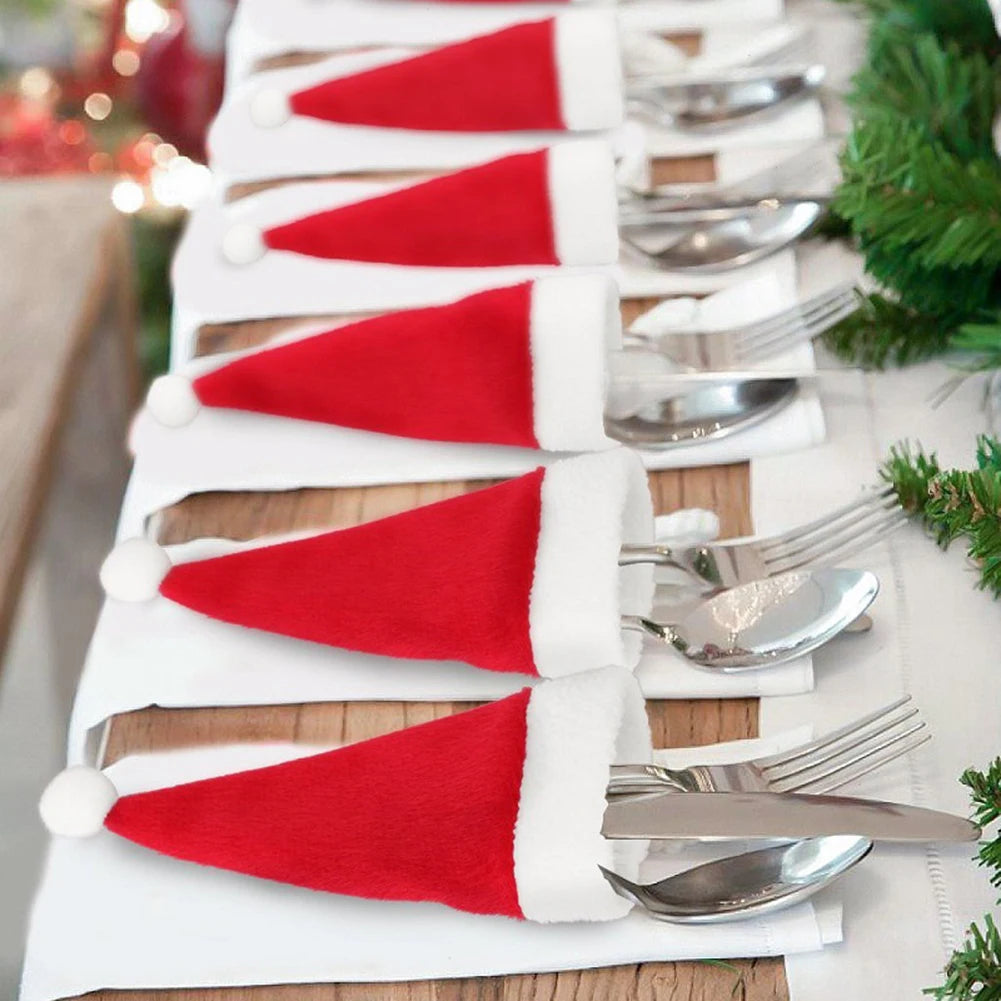 Set of cutlery with Santa hat napkins on a table with Christmas decorations.