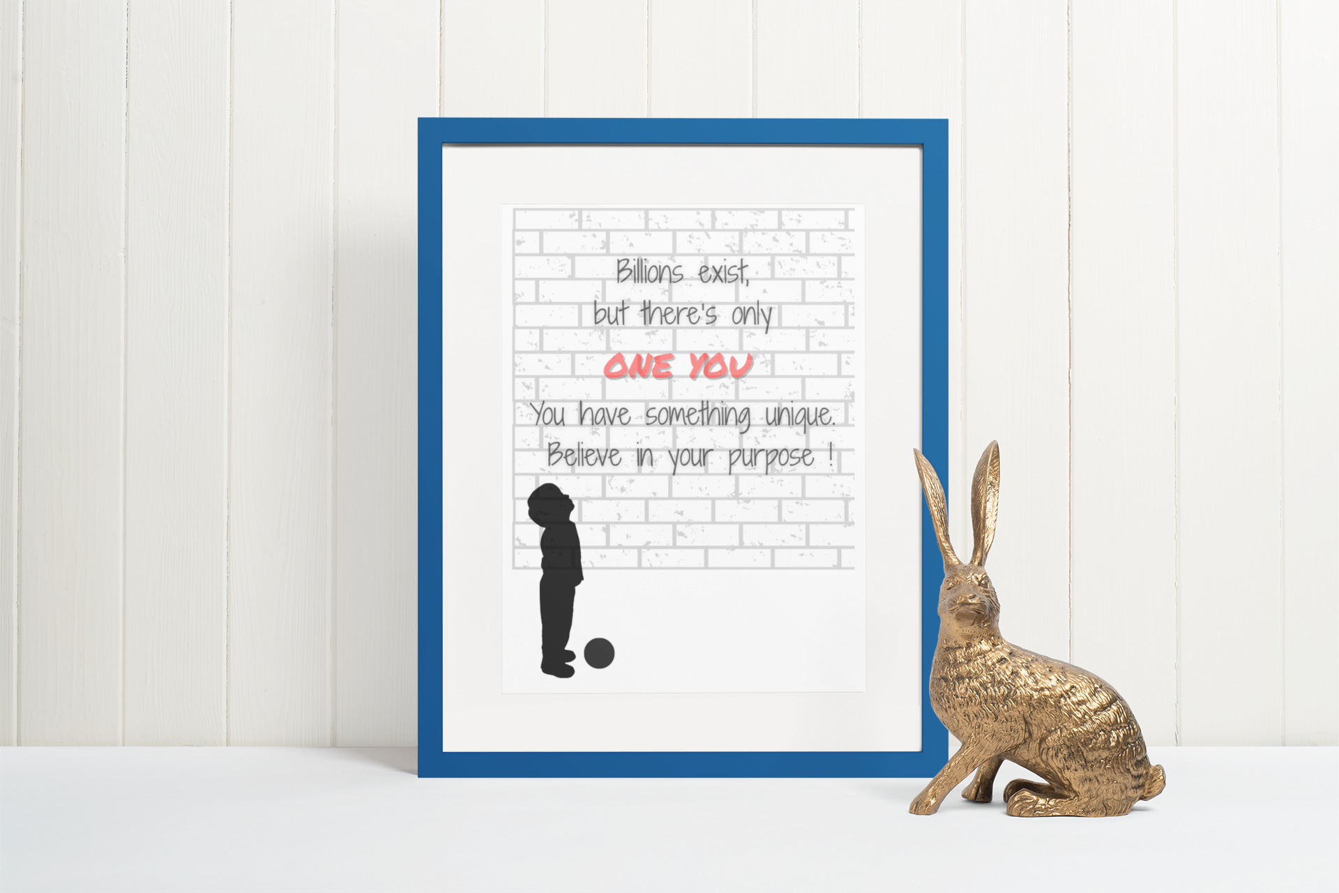 Framed motivational quote with silhouette of a person and a ball, on a white wall with a gold rabbit figurine.