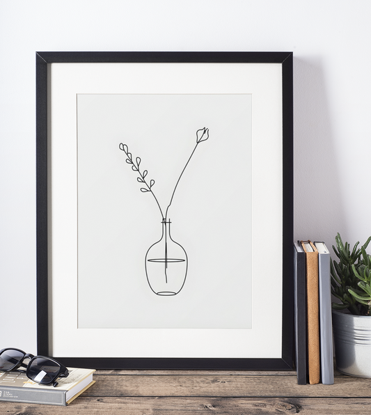 Framed line art print of a vase with a branch on a white wall.