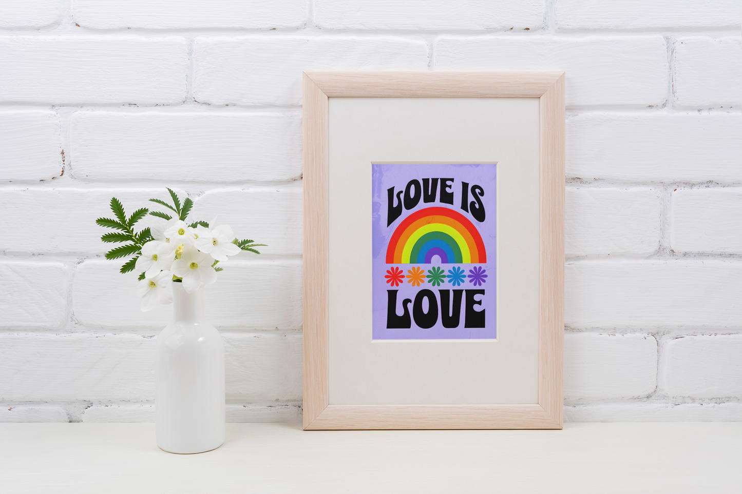 Framed artwork with 'Love is Love' message on a white brick wall background