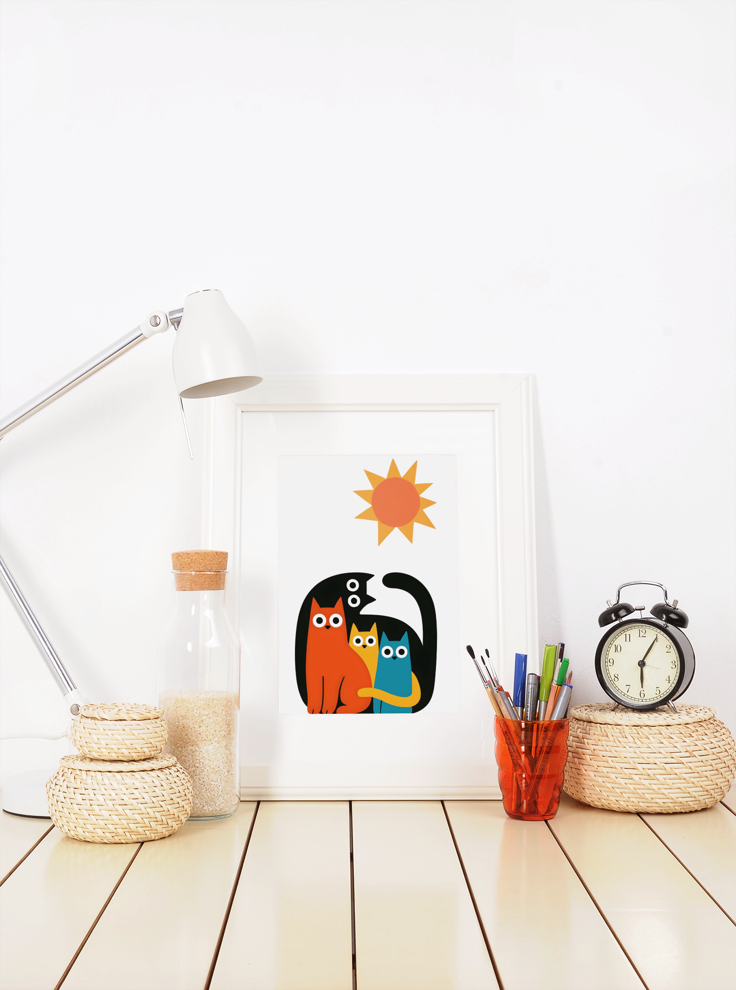 Framed cat family poster with sun – colorful minimalist art print displayed on desk with lamp, clock and stationery
