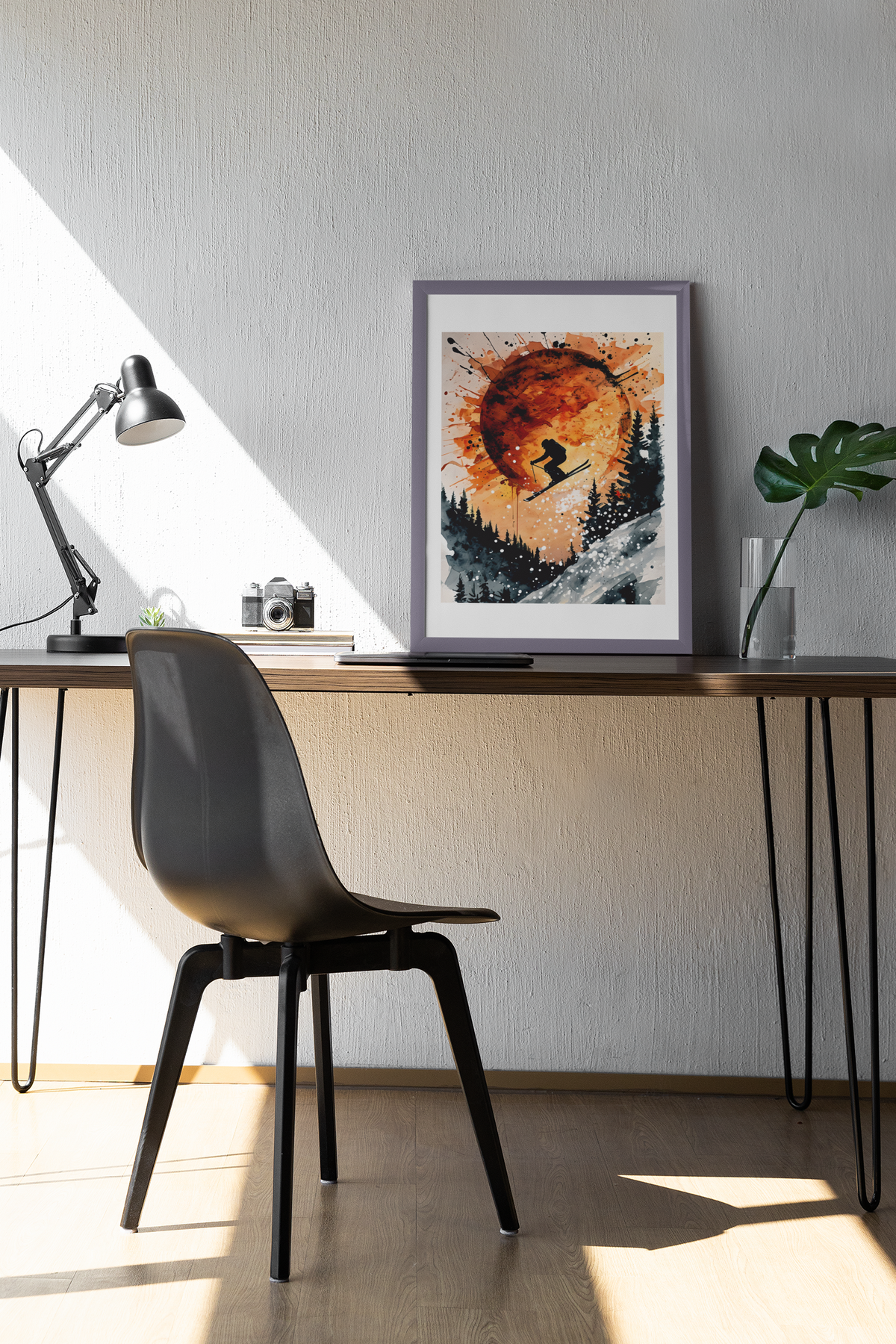 Framed sunset ski jump poster featuring skier silhouette and abstract orange sun, styled on a modern wooden desk with lamp, camera, and plant.