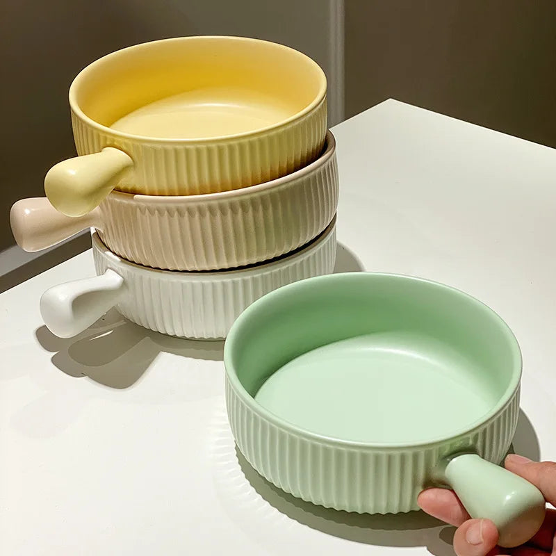 Set of colorful ceramic bowls with handles on a white surface.