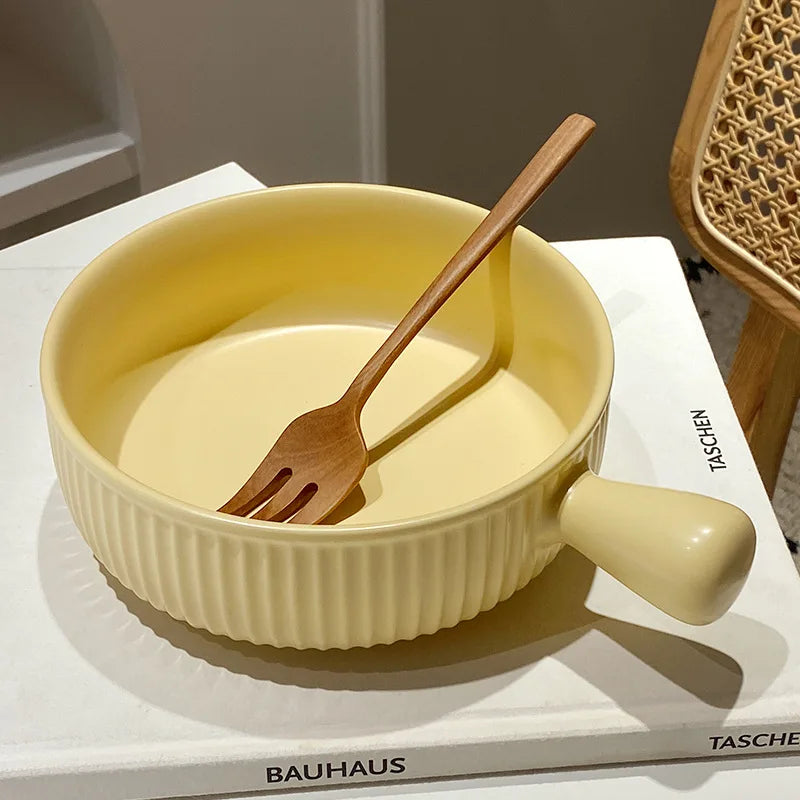 Yellow ceramic bowl with a wooden fork on a white surface with 'Bauhaus' and 'Taschen' branding.
