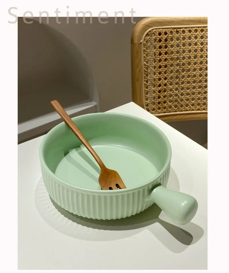 Light green ceramic bowl with wooden spoon on a white surface, with a wicker chair in the background.