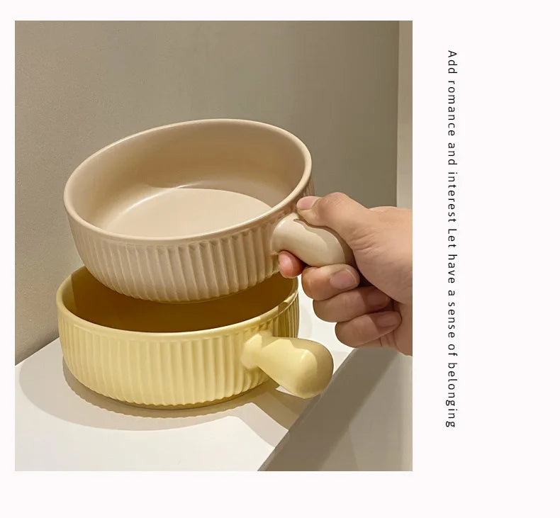 Hand holding two stacked ceramic bowls with handles on a neutral background