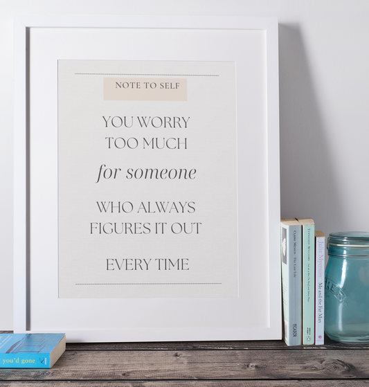Framed print with motivational quote on a shelf with books and a jar.