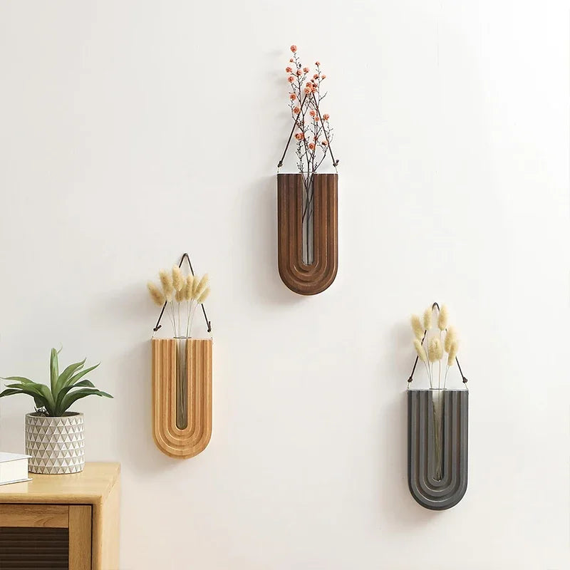 Three wall-mounted vases with plants on a light-colored wall.