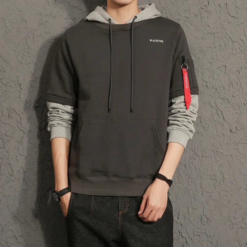 Person wearing a dark gray hoodie with a red patch on a gray background