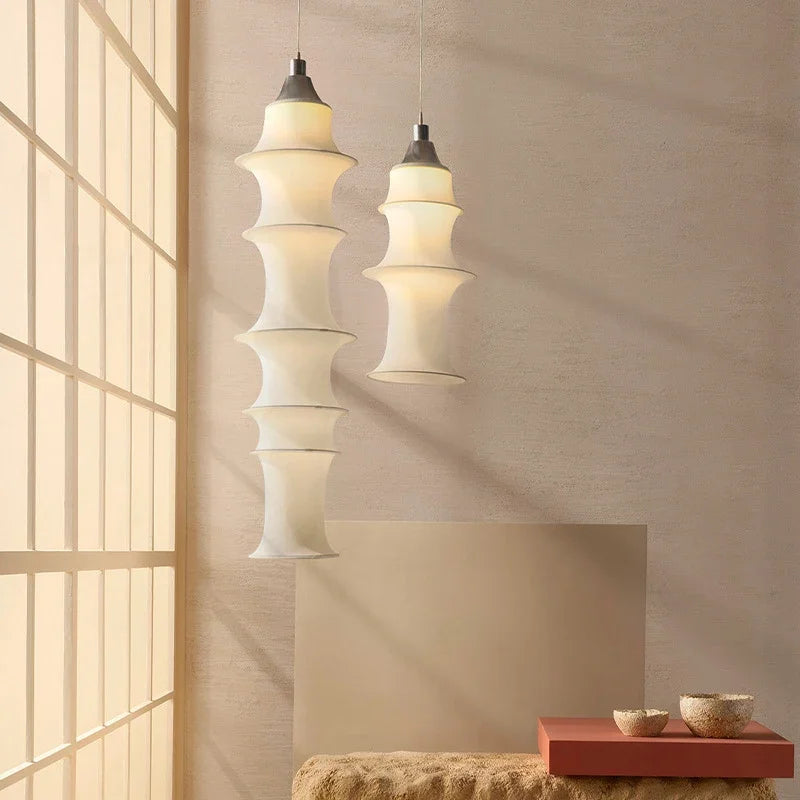 Two modern pendant lights hanging in a room with a textured wall and window.