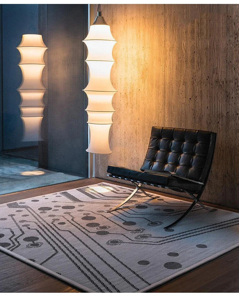 Modern interior with a patterned rug, black chair, and tall lamps.