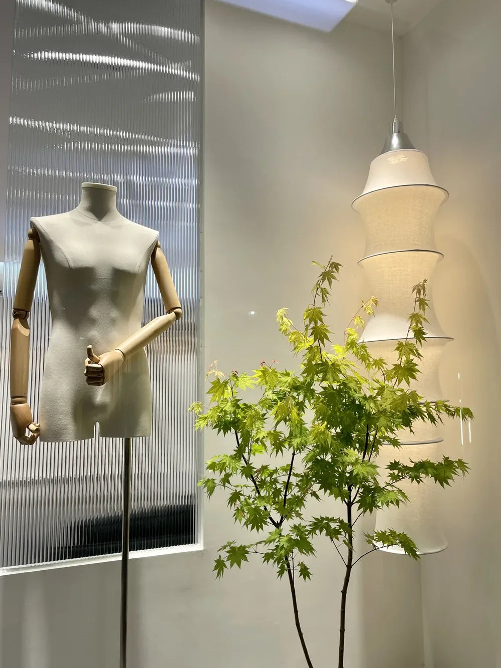 Mannequin against a glass wall with indoor plants and pendant lights in the background