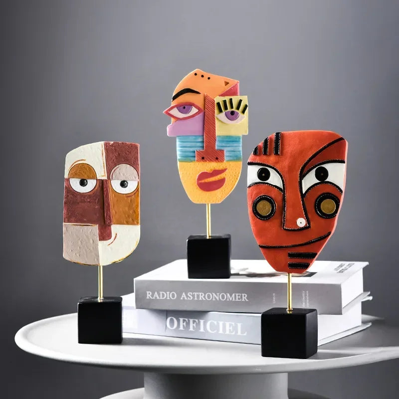 Three abstract face sculptures on books with a gray background