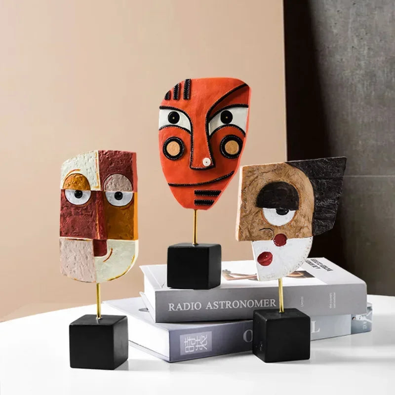 Three abstract face sculptures on books against a neutral background