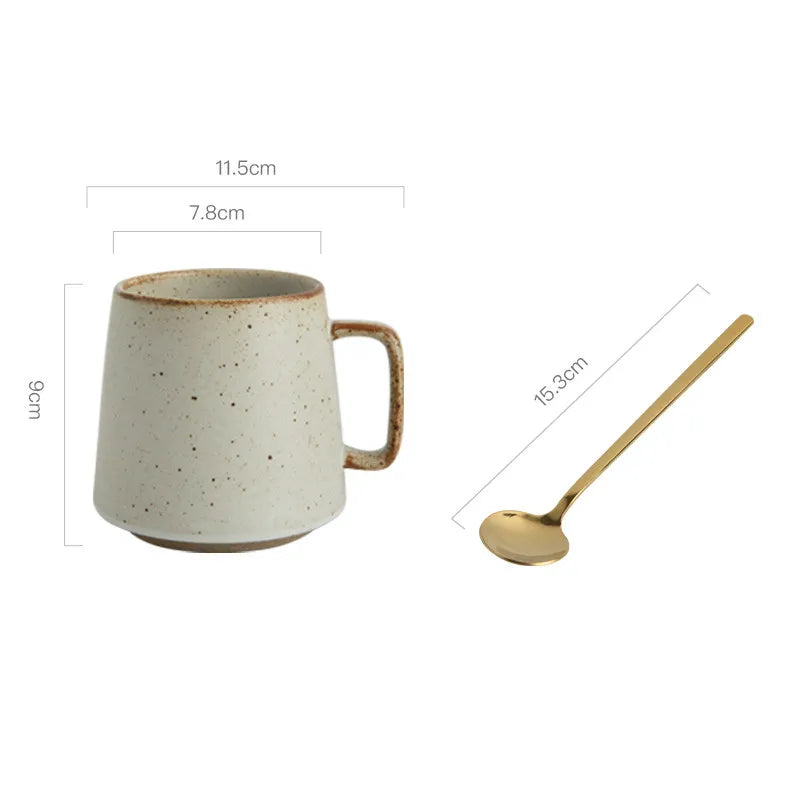 Ceramic mug with speckled pattern and gold spoon on a white background