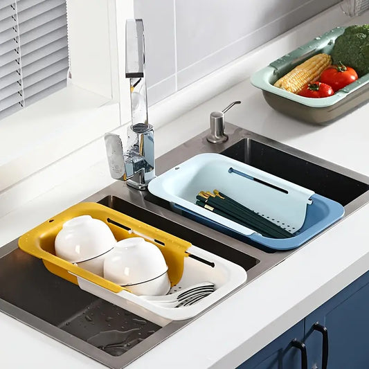 Kitchen sink with yellow and blue dish drying racks and a bowl of vegetables on a counter.
