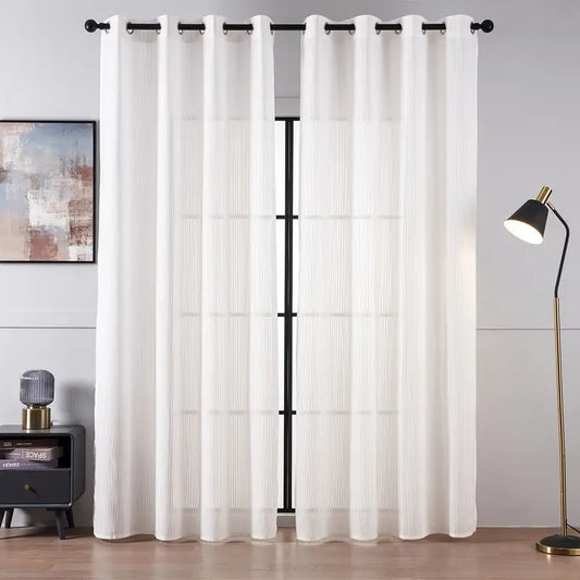 White curtains with black grommets hanging in a room with a lamp and side table.