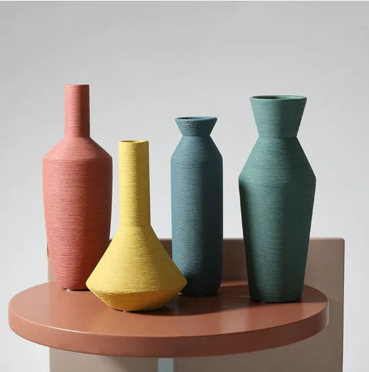 Four colorful vases on a round wooden table against a plain background